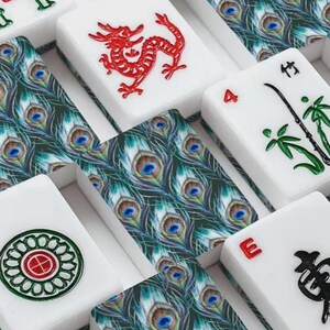 Puede incluir: Una colecci&oacute;n de fichas de mahjong rectangulares con superficies blancas y diversos dise&ntilde;os. Algunas fichas muestran intrincados patrones de plumas de pavo real verdes, mientras que otras presentan motivos de dragones rojos, s&iacute;mbolos de bamb&uacute; verdes, caracteres negros y un emblema circular.