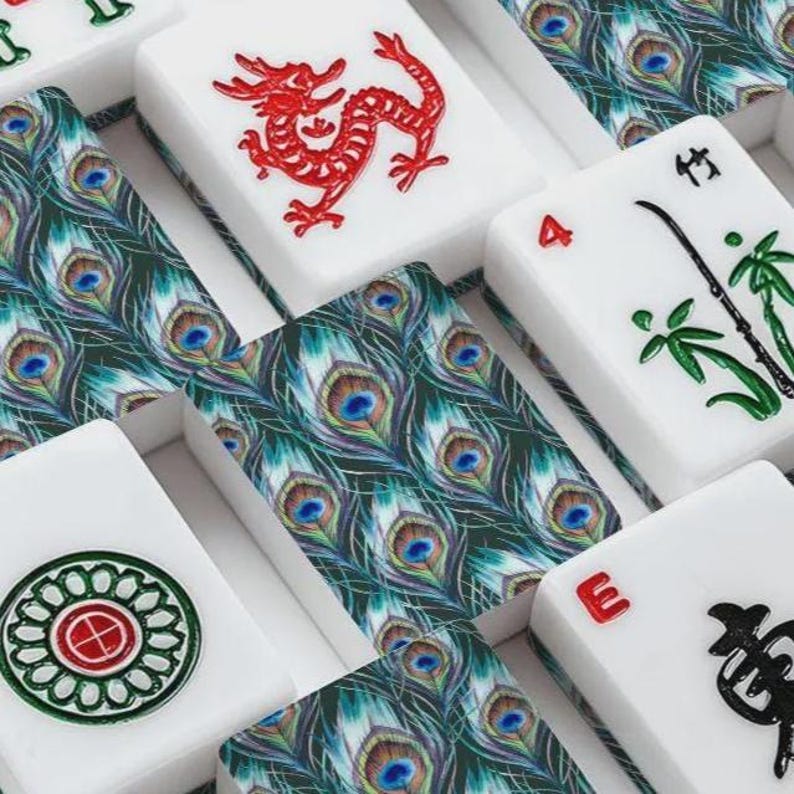Puede incluir: Una colecci&oacute;n de fichas de mahjong rectangulares con superficies blancas y diversos dise&ntilde;os. Algunas fichas muestran intrincados patrones de plumas de pavo real verdes, mientras que otras presentan motivos de dragones rojos, s&iacute;mbolos de bamb&uacute; verdes, caracteres negros y un emblema circular.