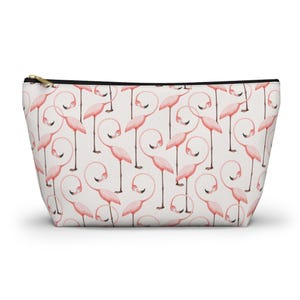 Puede incluir: Bolsa de cosméticos blanca con cremallera dorada, estampada con flamencos rosas. Los flamencos tienen cuellos curvos y están sobre un fondo blanco. Ideal para guardar maquillaje.
