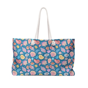 May include: A large tote bag featuring a blue background adorned with a seashell pattern in pink, yellow, and orange hues. It has white rope handles. The bag is rectangular in shape and designed for carrying items.
