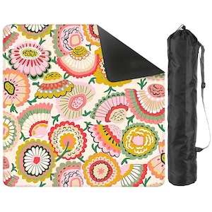 May include: A square outdoor blanket featuring a cream background with a repeating pattern of stylized flowers in shades of pink, yellow, green, and orange. The blanket has a black underside and includes a black cylindrical carrying bag with a strap.