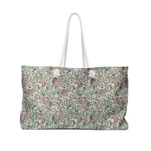Peut inclure: Grand sac fourre-tout avec un fond crème et un motif répété de visages de léopards et de feuillage vert. Le sac a des poignées en corde blanche et des accents blancs. Conçu pour transporter des articles.