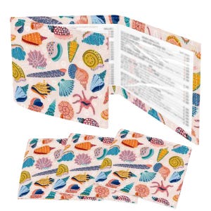May include: A wallet and coasters featuring a seashell pattern in shades of orange, blue, yellow, and pink on a light pink background. The wallet is open, revealing clear pockets. The coasters are stacked below the wallet.