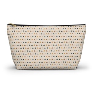 May include: A beige cosmetic bag with a repeating pattern of small triangles in shades of brown, green, and gold. The bag has a black zipper and a gold-colored zipper pull.
