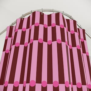 May include: A pink and brown striped shower curtain with pink polka dots. The curtain hangs from a curved, silver-colored rod. The design features alternating vertical stripes and evenly spaced circles.