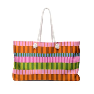 May include: A large tote bag with a vibrant striped design. The bag showcases vertical stripes in pink, orange, brown, green, and blue. It has white rope handles and white detailing where the handles are attached.