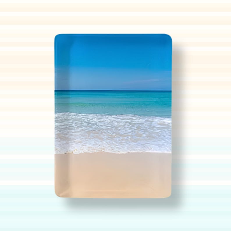 May include: A rectangular glass tray featuring a printed image of a beach scene. The design displays a light beige sandy shore, white sea foam from gentle waves, a turquoise ocean, and a clear blue sky, all captured in a smooth finish.