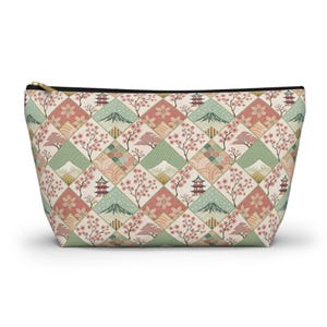 May include: A zipped pouch with a repeating pattern of Japanese-inspired motifs. The design features cherry blossoms, pagodas, mountains, and geometric shapes in pink, green, and beige. The zip is gold-toned.