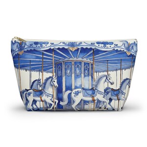 May include: A white cosmetic bag with a blue carousel design. The carousel features white horses with blue saddles and a blue and white canopy. The bag has a gold zipper and a white background.