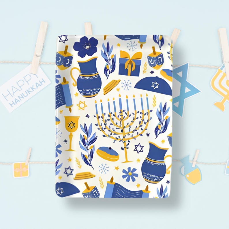 K&ouml;nnte beinhalten: Ein rechteckiges Stoffst&uuml;ck mit einem sich wiederholenden Muster aus blauen und goldenen Chanukka-Symbolen auf cremefarbenem Hintergrund. Das Design umfasst eine Menora, Dreidels, Kr&uuml;ge, Schriftrollen, Geschenke, Davidsterne und florale Elemente.