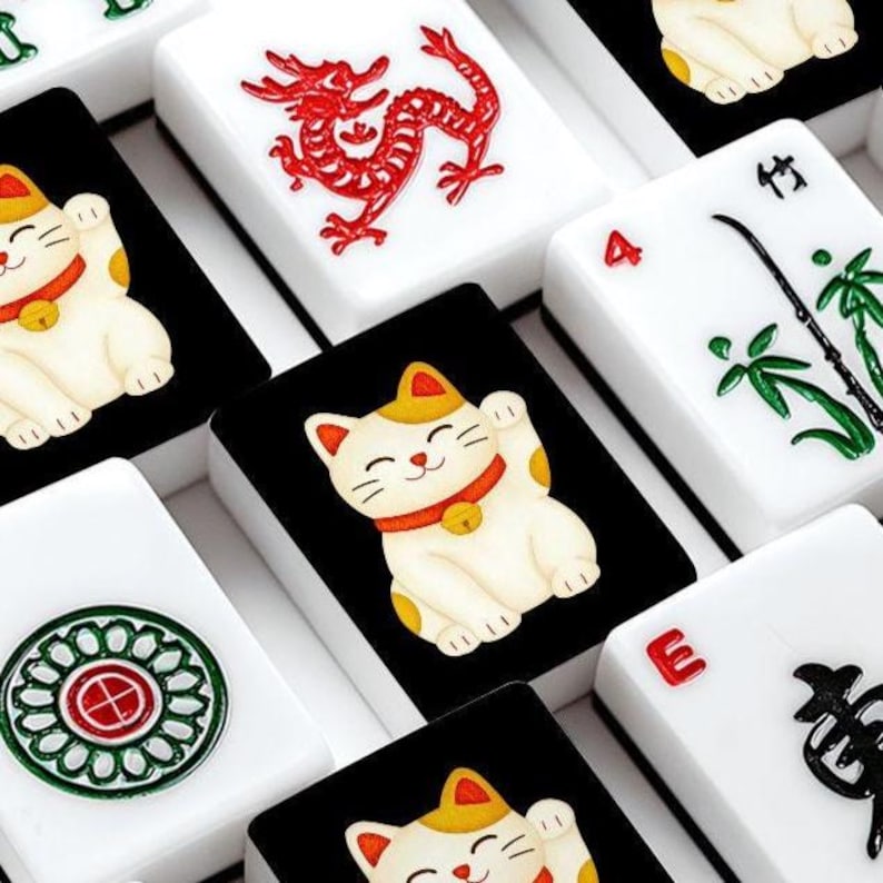 May include: Close-up of a set of Mahjong tiles. The tiles feature various designs, including a red dragon, a lucky cat, and bamboo. The tiles are white with black accents and colorful illustrations.