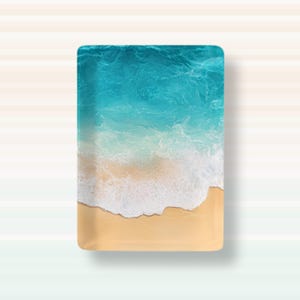 May include: A rectangular tray featuring a top-down view of a beach scene. The design displays a smooth, light tan sandy shore at the bottom, transitioning into white, foamy ocean waves, and deep turquoise blue water at the top of the tray.