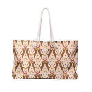 Peut inclure: Grand sac fourre-tout beige avec un motif répété de guépards, de lunes et d'étoiles. Le sac a des poignées en corde blanche et des accents blancs. Conçu pour transporter des articles.
