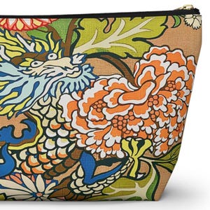 May include: A zipped pouch featuring a vibrant, multi-coloured print on a tan background. The design displays a stylised dragon with blue and white scales, surrounded by large orange and white peony flowers and bright green foliage.