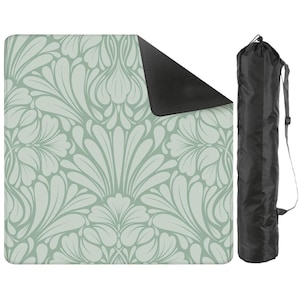 May include: A light green and white floral patterned picnic blanket with a black underside. A black carrying bag with a shoulder strap is next to the blanket. The blanket is designed for outdoor use.