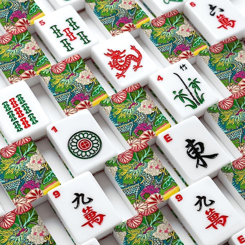 May include: A close-up of a Mahjong set with white tiles. The tiles display numbers, symbols, and Chinese characters in red and black. Some tiles have a colourful floral and dragon design.
