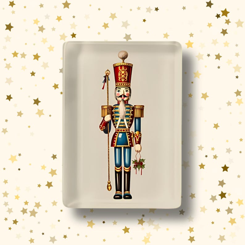 May include: A rectangular off-white ceramic tray featuring a central illustration of a nutcracker soldier. The soldier wears a red and blue uniform with gold accents, a tall hat, and holds a long gold staff and a small sprig of green holly berries.