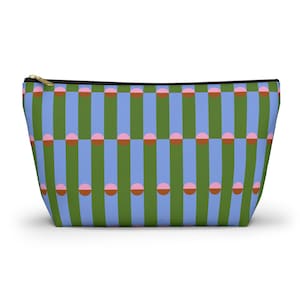 May include: A rectangular cosmetic bag with a colorful geometric pattern. The design features vertical stripes in green and light blue, with alternating pink and brown half-circles. The bag has a black zipper and a gold-colored pull.