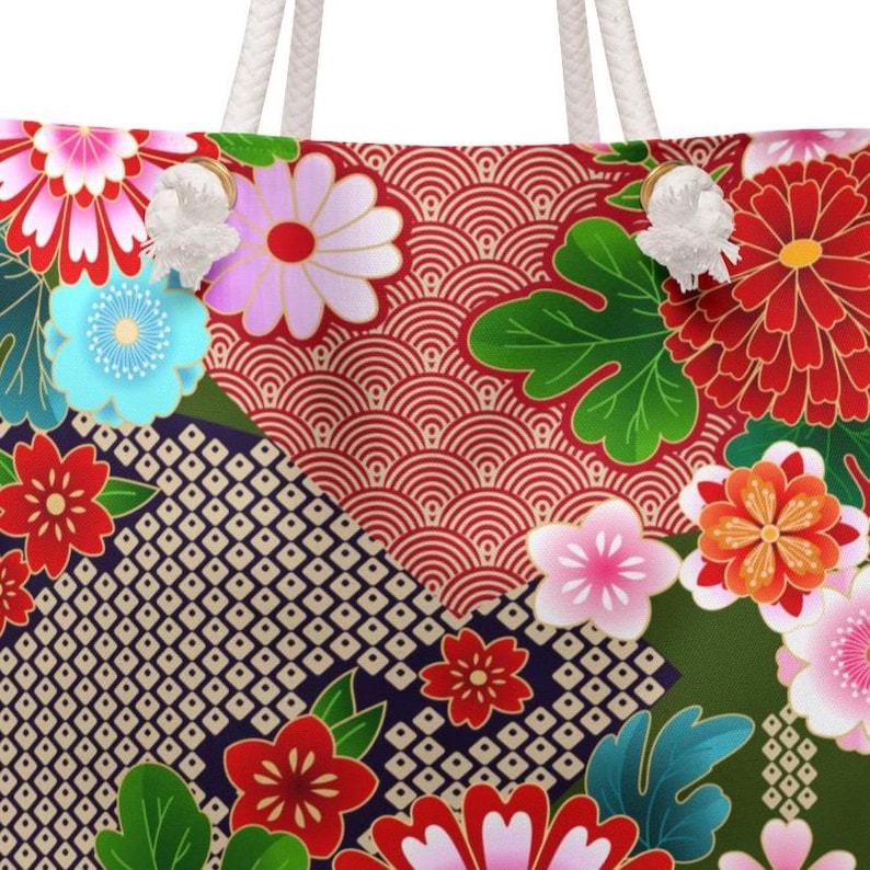 May include: A tote bag featuring a vibrant Japanese-inspired floral pattern with red, pink, orange, and blue flowers, green leaves, and geometric wave and diamond motifs. The bag includes thick, white braided rope handles attached with metal grommets.