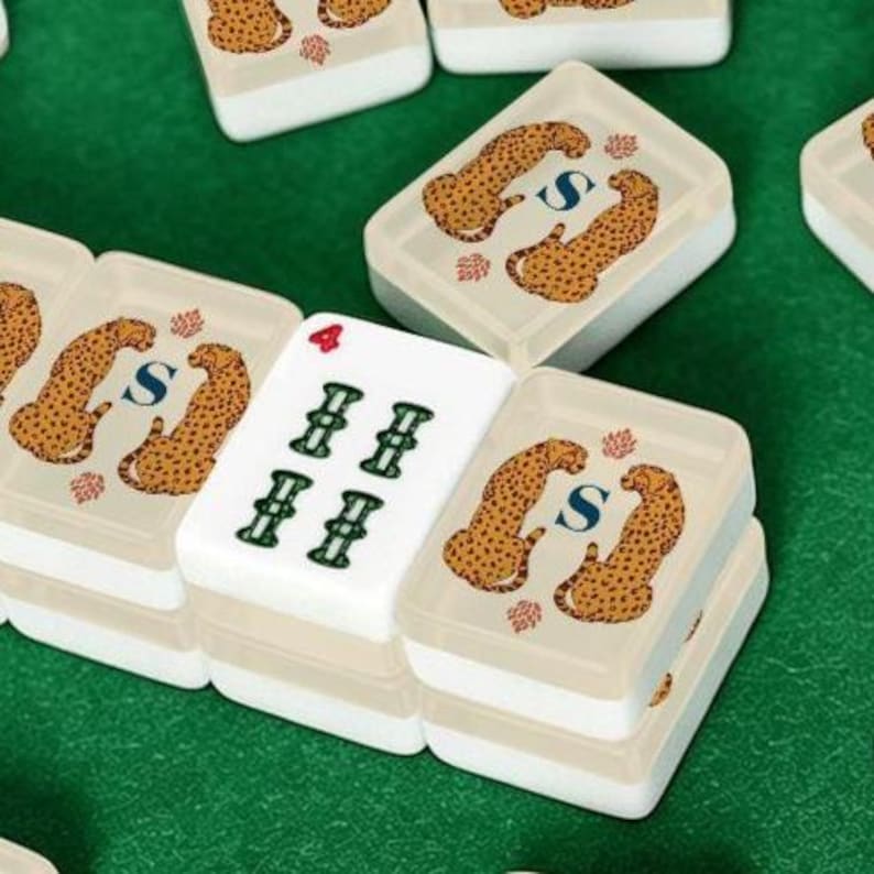May include: A set of rectangular mahjong tiles with a white base. Several tiles feature a graphic of two spotted leopards flanking a blue letter S. One central tile displays a red number 4 and four green symbols arranged in a grid pattern.