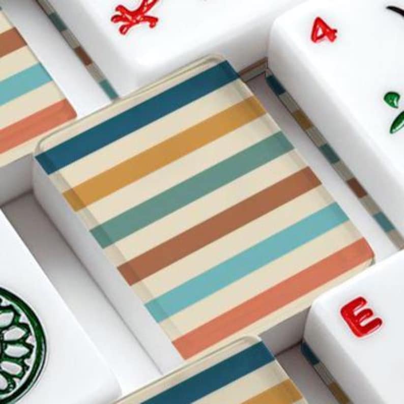 Pode incluir: Uma pe&ccedil;a retangular de mahjong com um padr&atilde;o repetitivo de listras horizontais em tons de azul escuro, amarelo mostarda, azul-petr&oacute;leo e laranja terracota sobre um fundo creme, rodeada por outras pe&ccedil;as brancas com marca&ccedil;&otilde;es vermelhas e verdes.