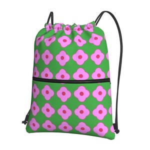 May include: A green drawstring bag featuring a repeating pattern of pink flower shapes. The bag has a black zip and black drawstring straps. The bag is made of a lightweight fabric.
