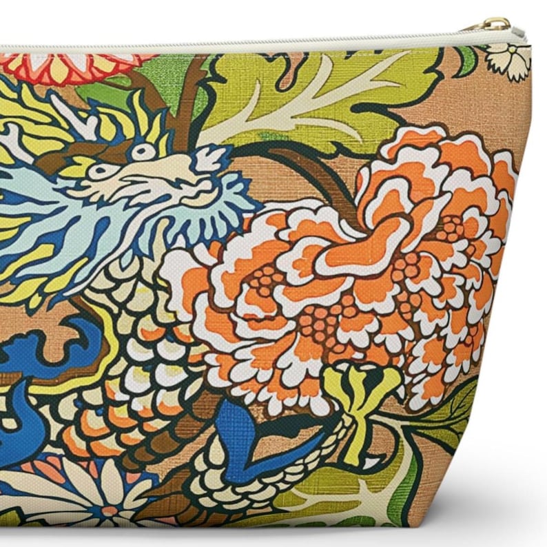 May include: A zipped pouch featuring a vibrant, multi-coloured print of a dragon with blue, yellow, and white scales, surrounded by large orange and white peony flowers and green foliage against a textured, light brown background.