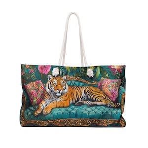 May include: A large tote bag with a striking design. It depicts a tiger resting on a teal sofa with floral cushions, set against a backdrop of lush foliage. The bag has a white rope handle.