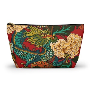 May include: A zippered pouch featuring a vibrant dragon and floral pattern. The design includes a red background with a teal, yellow, and orange dragon, and large yellow flowers. The pouch has a black zipper and is likely used for cosmetics or travel.