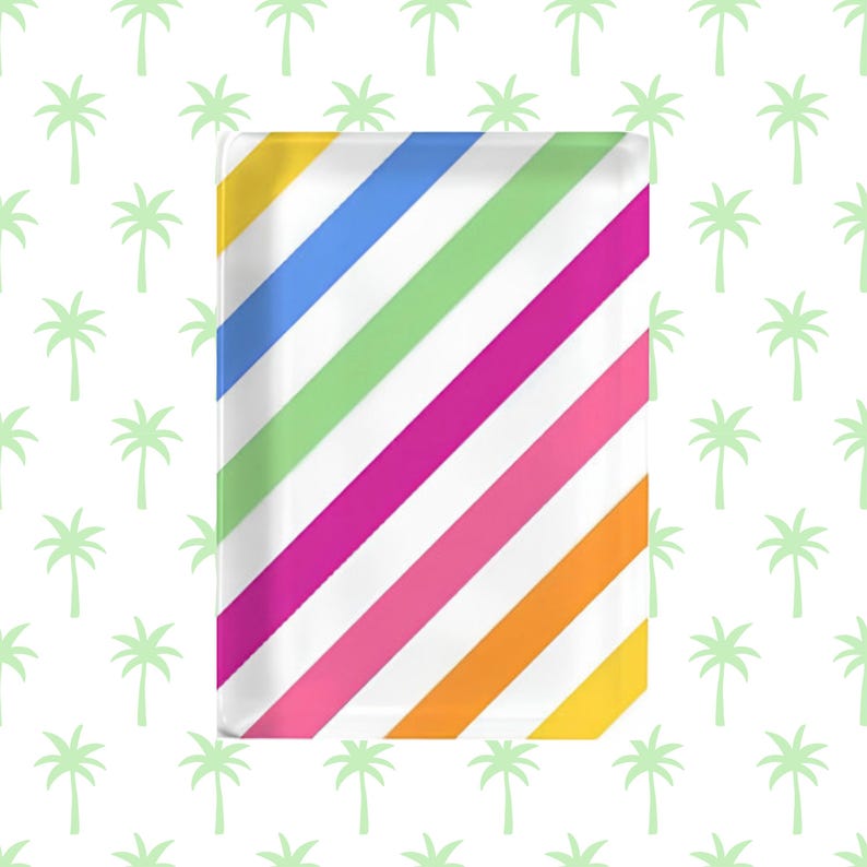 K&ouml;nnte beinhalten: Ein rechteckiges Tablett mit einem lebendigen Muster aus diagonalen Streifen in Gelb, Blau, Hellgr&uuml;n, Magenta, Pink und Orange auf wei&szlig;em Grund. Die Oberfl&auml;che ist glatt und gl&auml;nzend und zeigt ein sich wiederholendes Regenbogen-Design.