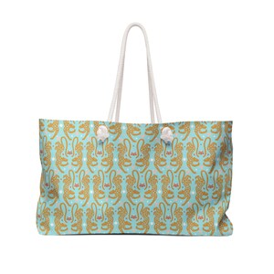 Peut inclure: Grand sac fourre-tout avec un fond bleu clair et un motif répété de guépards dorés. Le sac a des poignées en corde blanche et des accents blancs. Les guépards sont stylisés avec des détails floraux.