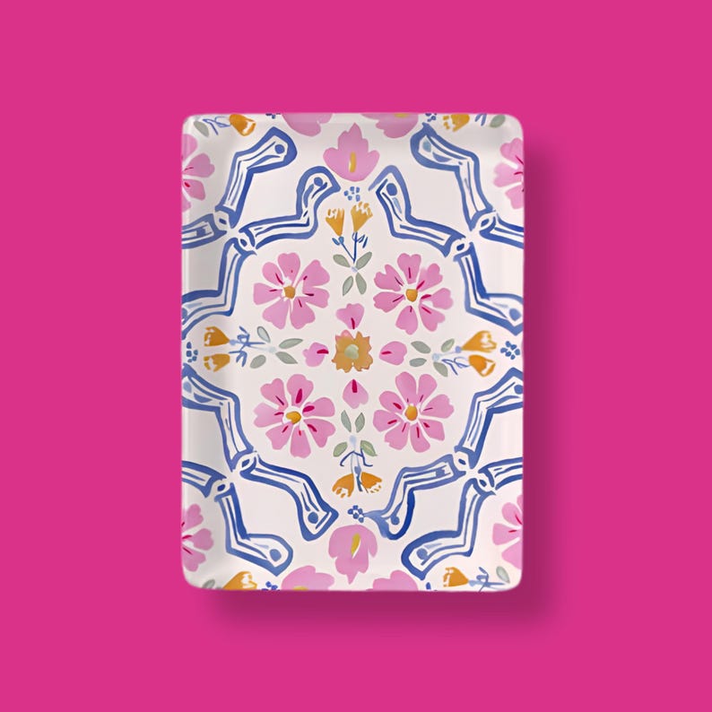May include: A rectangular ceramic tray featuring a white background with a repeating pattern of pink flowers, yellow buds, and blue wavy lines. The design is symmetrical, showcasing a central floral arrangement surrounded by blue geometric accents.