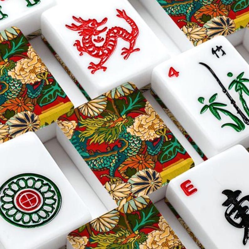 Puede incluir: Una colecci&oacute;n de fichas de mahjong rectangulares con superficies blancas y dise&ntilde;os grabados. Algunas fichas muestran dragones rojos, tallos de bamb&uacute; verdes o patrones circulares, mientras que otras presentan un estampado floral y de drag&oacute;n multicolor.