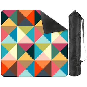 May include: A square outdoor blanket featuring a geometric pattern of triangles in shades of orange, teal, yellow, pink, and dark blue, with a black underside and a matching black cylindrical carrying bag with an adjustable shoulder strap.