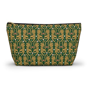 Peut inclure: Une trousse zippée avec un motif répété de guépards dorés, de fleurs roses et d'étoiles blanches sur un fond vert foncé. La trousse a une fermeture éclair noire et est probablement utilisée pour les cosmétiques ou les voyages.