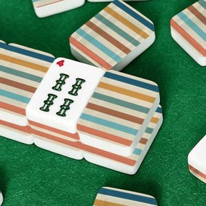 Pode incluir: Um conjunto de pe&ccedil;as retangulares de mahjong com base branca e um padr&atilde;o repetitivo de finas listras horizontais em tons de azul, bege e marrom. Uma pe&ccedil;a exibe o n&uacute;mero quatro em vermelho e quatro s&iacute;mbolos de bambu na cor verde.