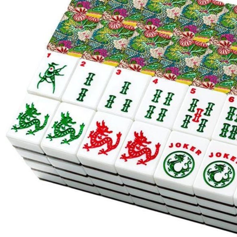 May include: A stack of white Mahjong tiles with green, red, and black symbols and numbers. The tiles feature dragon and joker designs. The set includes a patterned fabric with floral and dragon motifs.
