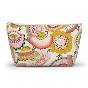 May include: A zippered pouch featuring a cream-colored background with a repeating pattern of stylized flowers in shades of mustard yellow, soft pink, coral, and sage green. The pouch has a gold-toned metal zipper pull at the top right corner.
