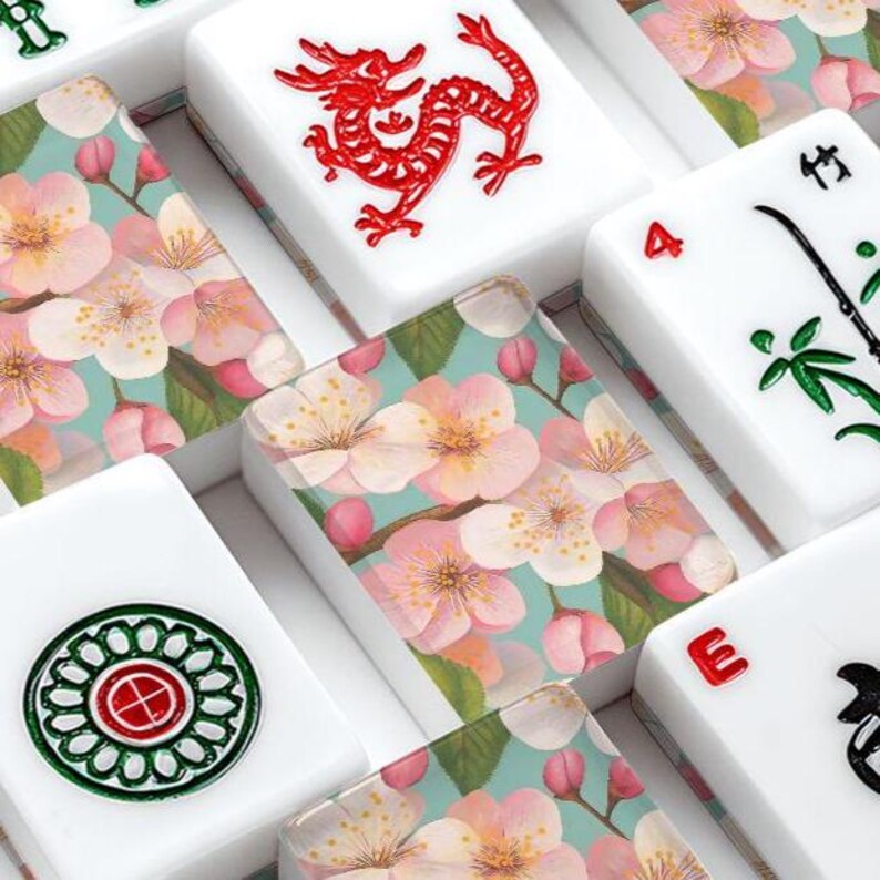 May include: Close-up of a Mahjong set with white tiles. Some tiles feature a red dragon, green and red circular design, and the number 4. Other tiles have a floral design with pink blossoms and green leaves.