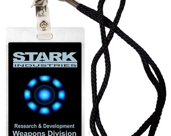 Peut inclure: Un porte-badge rectangulaire avec un cordon noir arborant le logo Stark Industries, un graphique de réacteur à arc bleu brillant et le texte Research & Development Weapons Division, incluant un code-barres et une attache métallique.