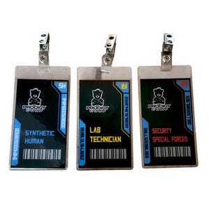Könnte beinhalten: Drei Ausweise mit Metallclips. Jeder Ausweis hat einen schwarzen Hintergrund mit weißem Text und einem Bärenlogo. Die Ausweise lauten "Synthetic Human", "Lab Technician" und "Security Special Forces".