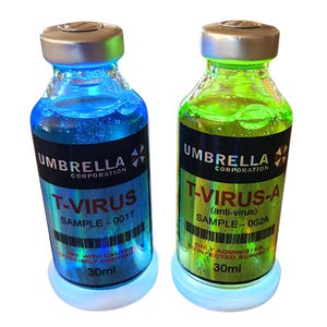 May include: Two glass vials with silver caps and glowing bases. One vial contains blue liquid, labeled "T-VIRUS." The other contains green liquid, labeled "T-VIRUS-A (anti-virus)." Both are marked "UMBRELLA CORPORATION" and "30ml."