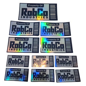 May include: A selection of holographic stickers. Each sticker features the text "Property Of RobCo INDUSTRIES" in a bold font, with a barcode design. The stickers have a reflective, iridescent finish, creating a shimmering effect.