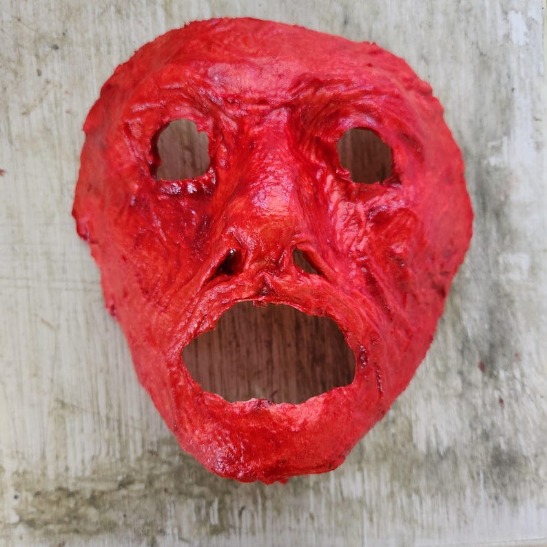 Puede incluir: Una m&aacute;scara de Halloween roja texturizada con una boca abierta de par en par y dos agujeros para los ojos.