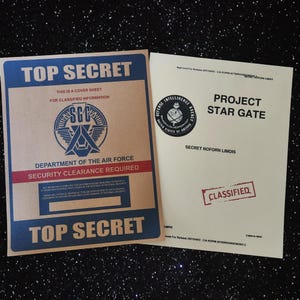 May include: Two brown and beige paper documents with the text "TOP SECRET" and "PROJECT STAR GATE" in black. The top document has a red seal with the text "SGC" and the text "DEPARTMENT OF THE AIR FORCE" and "SECURITY CLEARANCE REQUIRED". The bottom document has a white seal with the text "DEFENSE INTELLIGENCE AGENCY" and the text "SECRET NOFORN LIMDIS" and "CLASSIFIED".