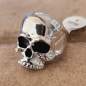 May include: A silver skull ring with black eye sockets. The ring is size 6.