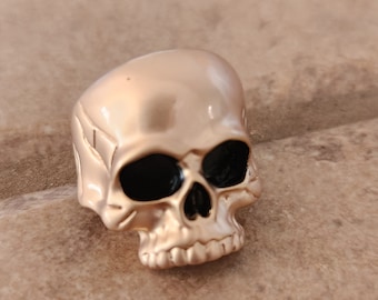 May include: A gold-colored skull ring with black eye sockets.