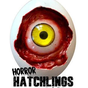 May include: A white eggshell with a yellow and black eyeball peeking out of a bloody, red interior. The text "HORROR HATCHLINGS Eyeball Eggs" is printed in black below the egg.