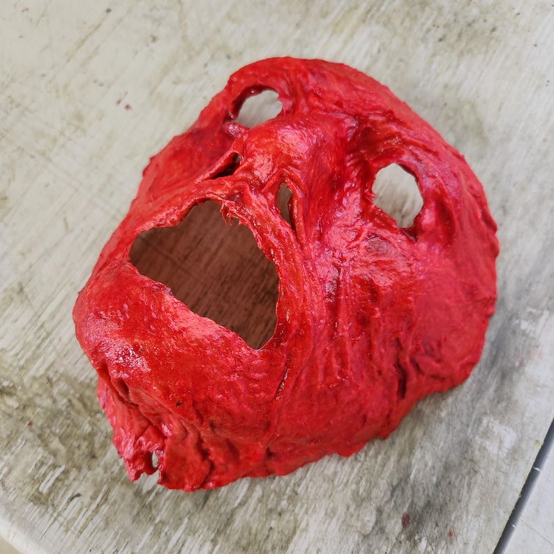 Puede incluir: Una m&aacute;scara roja, texturizada, de goma con dos agujeros para los ojos y una gran abertura para la boca. La m&aacute;scara est&aacute; dise&ntilde;ada para parecer una cara gritando.