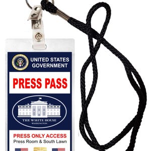 May include: A white plastic press pass with a black lanyard. The pass features the Presidential Seal, the words "United States Government", "Press Pass", and "The White House". It also includes the text "Press Only Access", "Press Room & South Lawn", and two American flags.